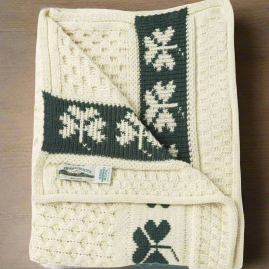 Folded Aran Shamrock Baby Blanket showing cable knit texture and green shamrock border detail.