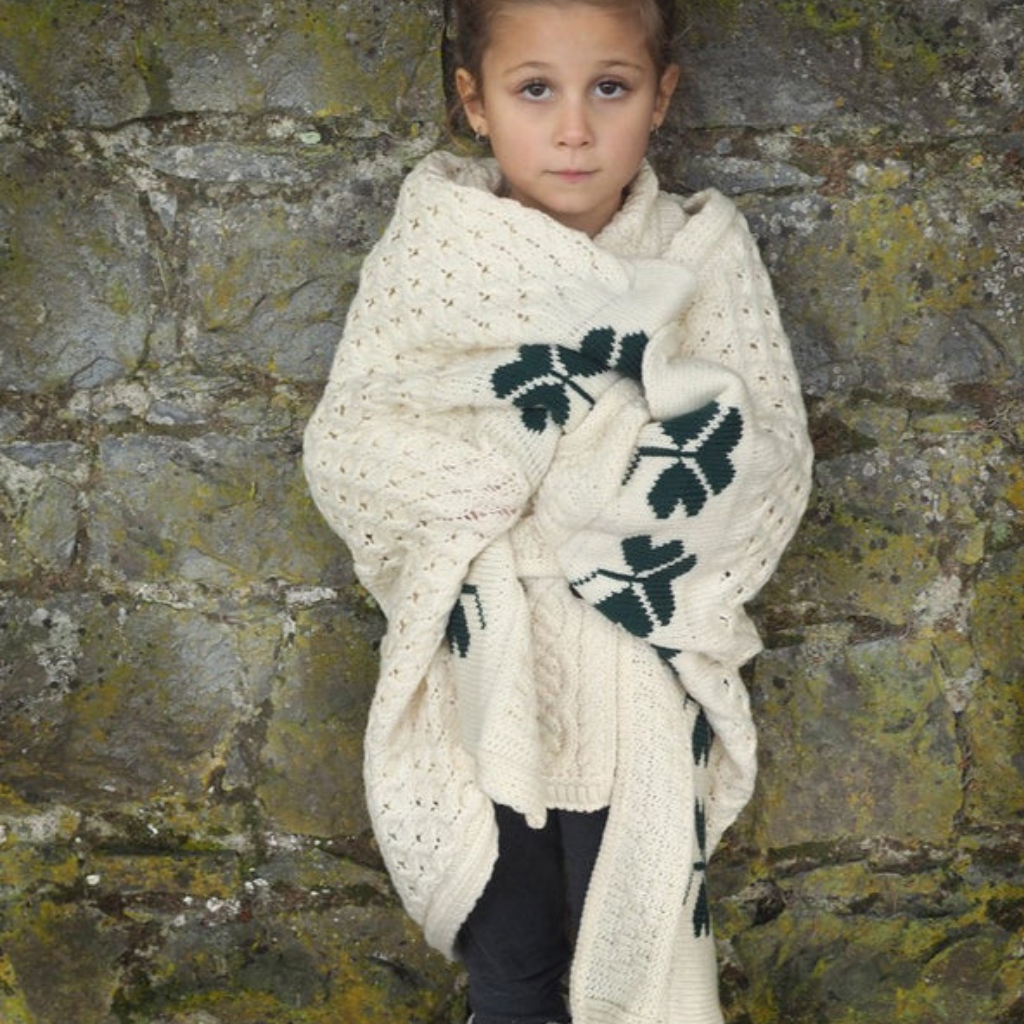 Child wrapped in Aran Shamrock Baby Blanket featuring traditional cable stitching and green shamrock pattern.