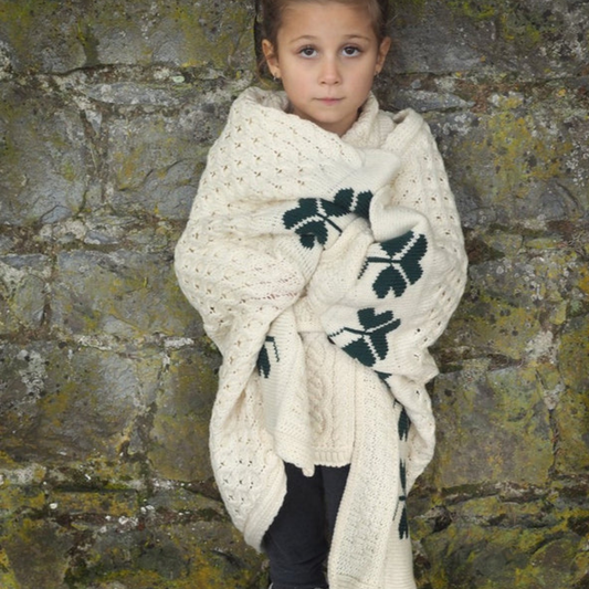 Child wrapped in Aran Shamrock Baby Blanket featuring traditional cable stitching and green shamrock pattern.