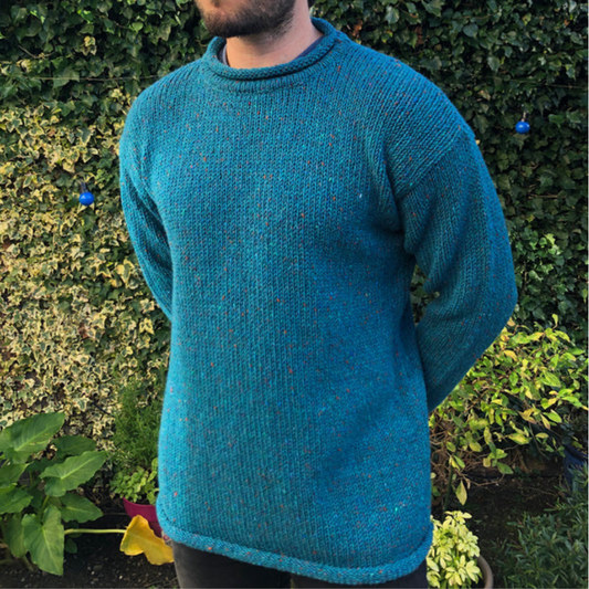 Man wearing turquoise Donegal roll neck Aran sweater, outdoors against green ivy background