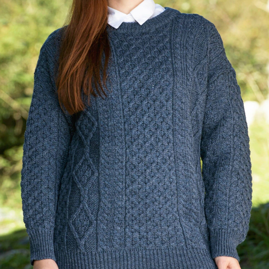 Woman wearing denim blue crew neck Aran sweater with traditional Irish stitches, made from 100% merino wool